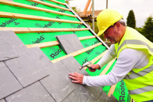 Male roofer in high vis jacket working with tiles and tools on a roof structure