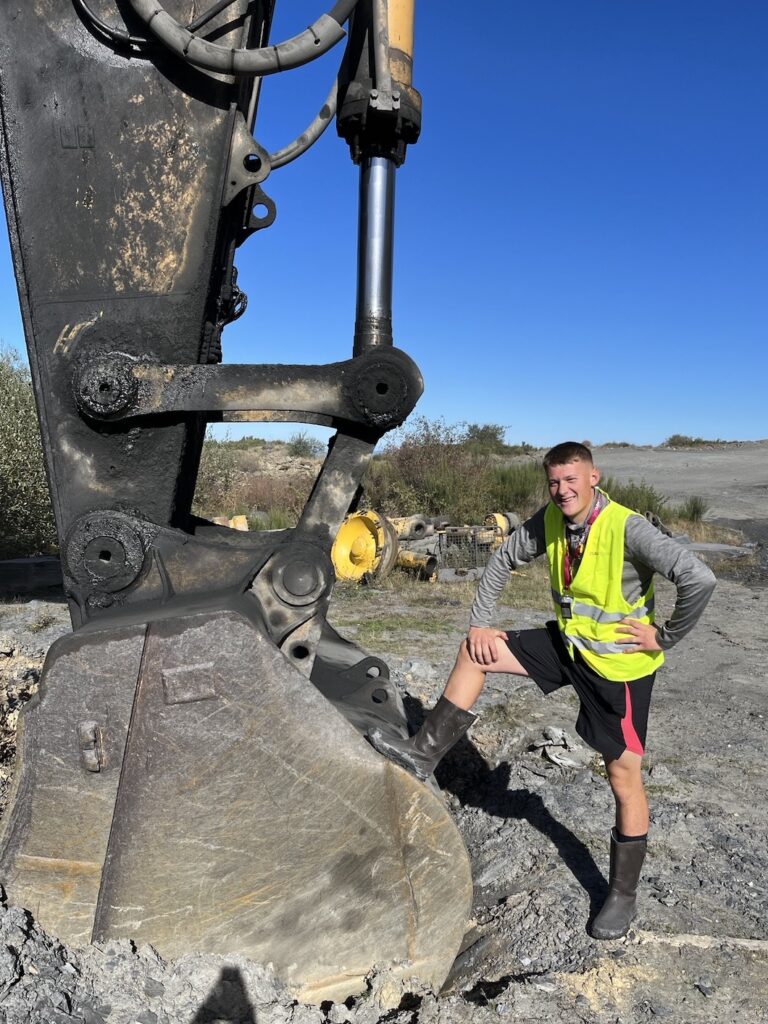 Sam Edwards stands in high vis and work boots stands at the foot of quarry machinery