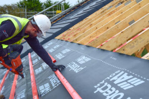 A roofing contractor is seen installing solar roofing underlay upon a roofing rig