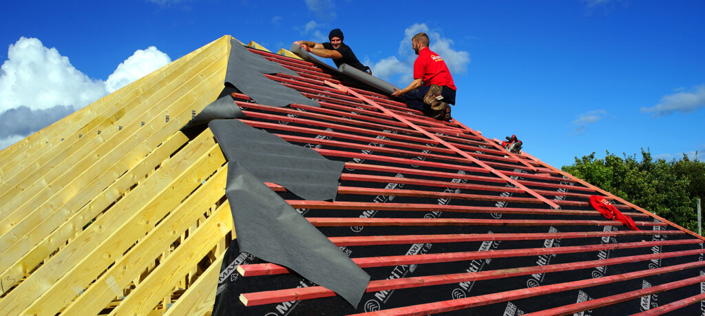 Roofers working on a new timber frame house. Fixing the felt and battens, prior to Slates being fitted. Photographed in October 2016.