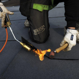 Flat roofing flame torch is being operated by an individual wearing protective gloves