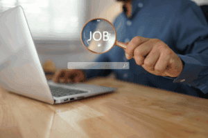 Magnifying glass held by a man at a laptop over the word job.