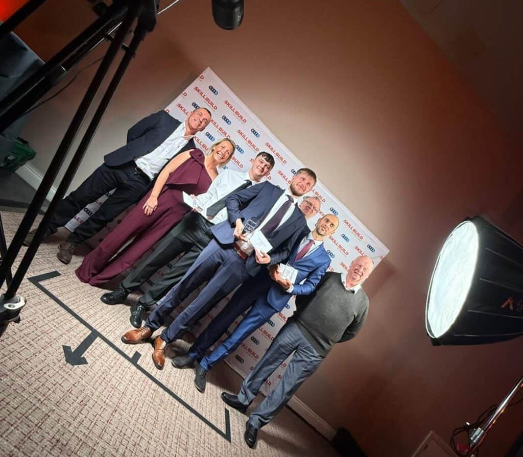 Three SkillBuild Winners stood with sponsors in front of a photo wall. 