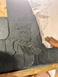 Paper template with design overlaying slates which have are being positioned and shaped to form the image.